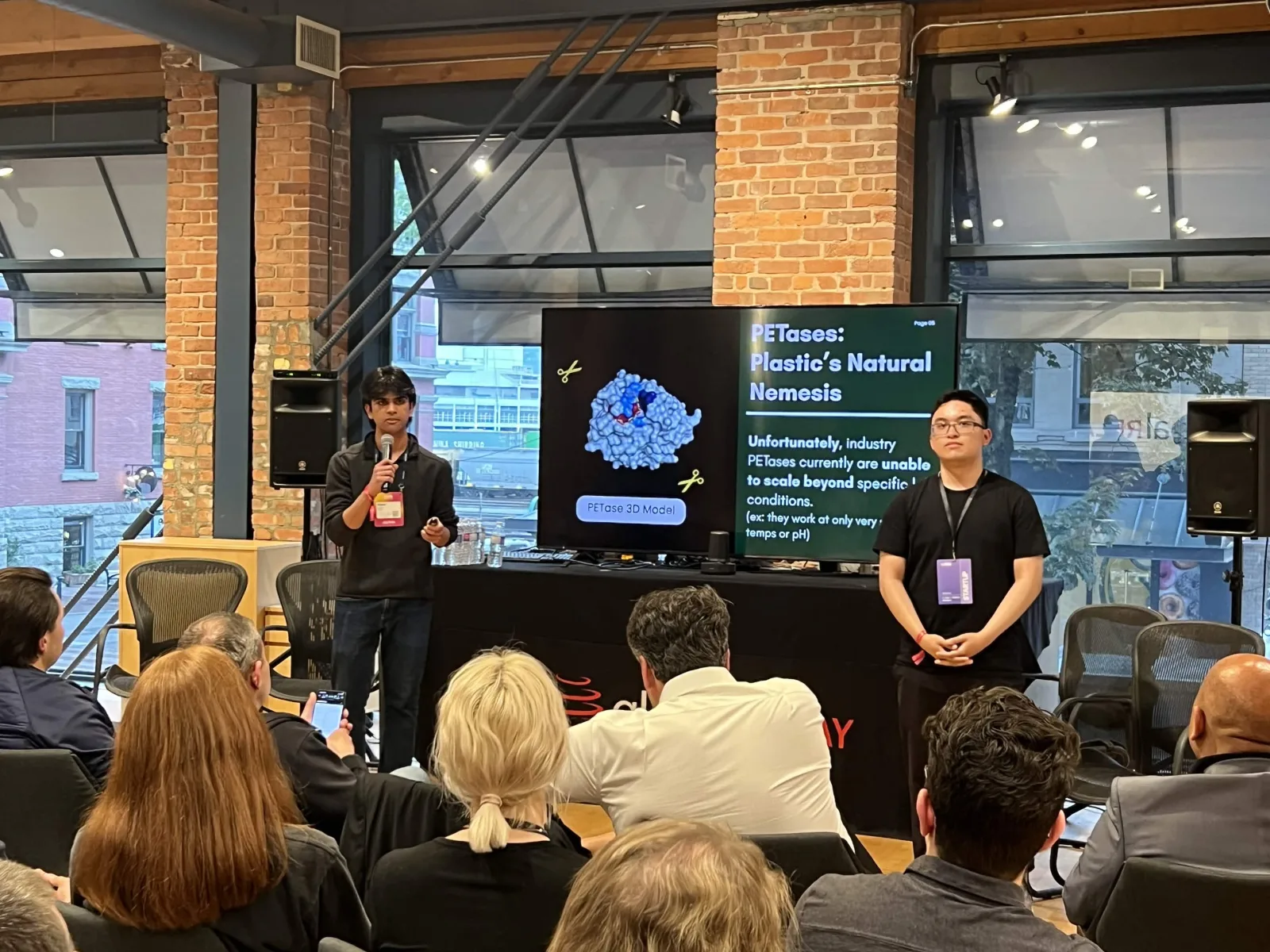 Team presents PETase enzyme research on stage at an industry demo day, May 2026